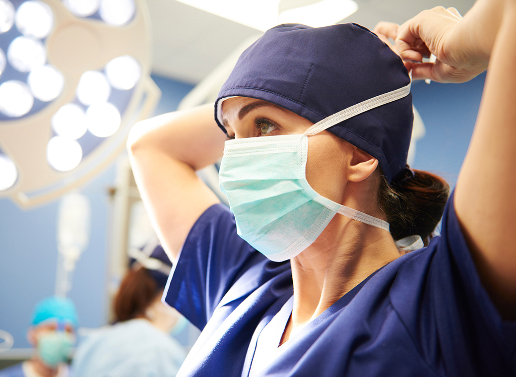 Surgeon in operating room preparing for anesthesia procedure by adjusting mask and surgical cap