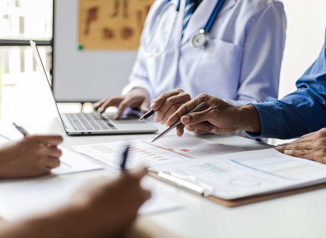 Doctor and professional reviewing financial charts and data on laptop and paperwork